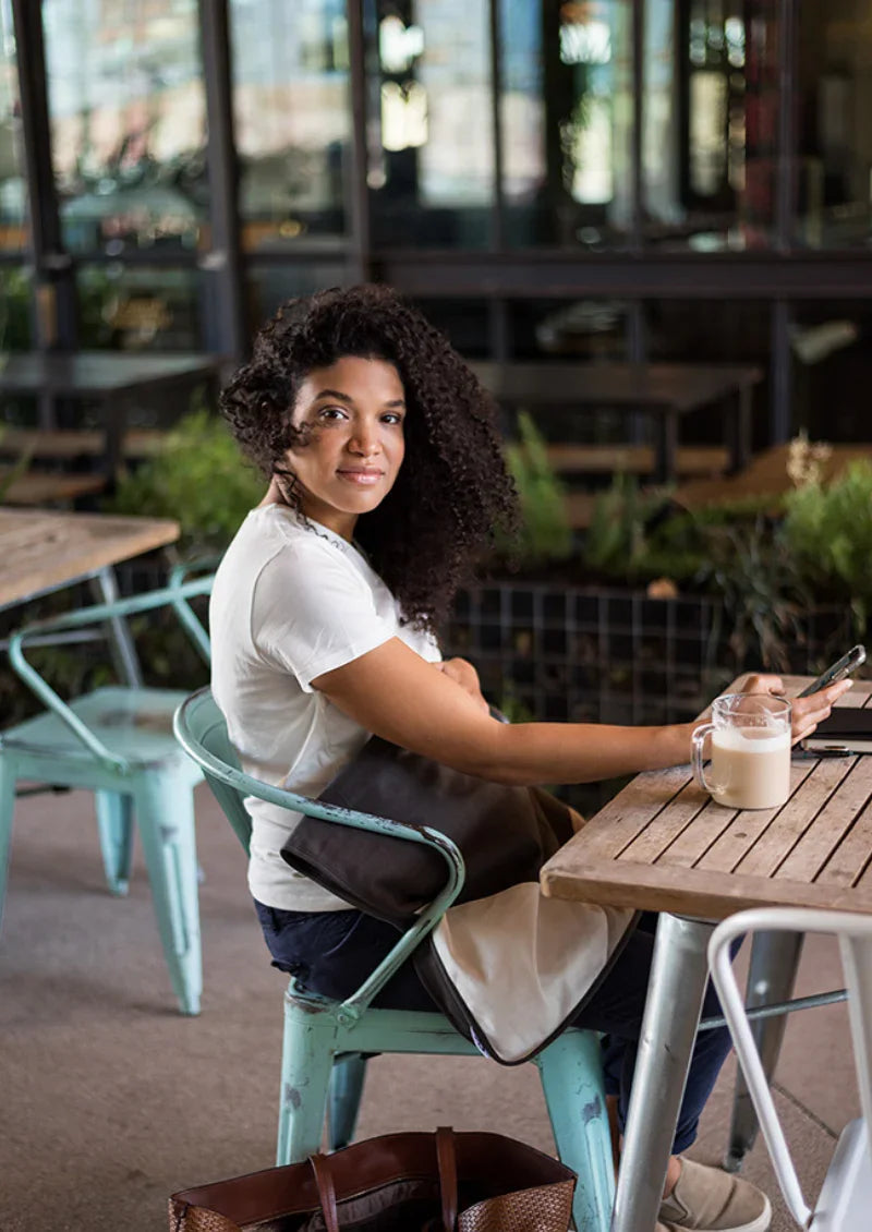 Woman seated at a cafe wearing a Mountain Charcoal Belly Armor blanket over her lap