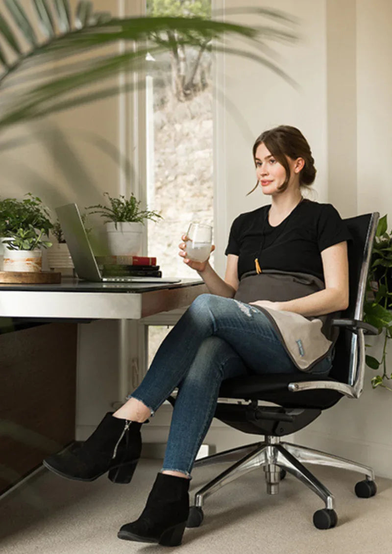 Pregnant woman seated at a desk with a charcoal Belly Armor blanket over her belly