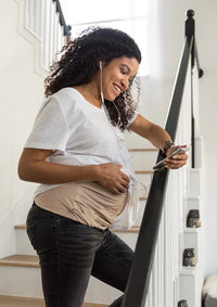 Pregnant woman using her phone while wearing an adjustable Belly Armor EMF belly band