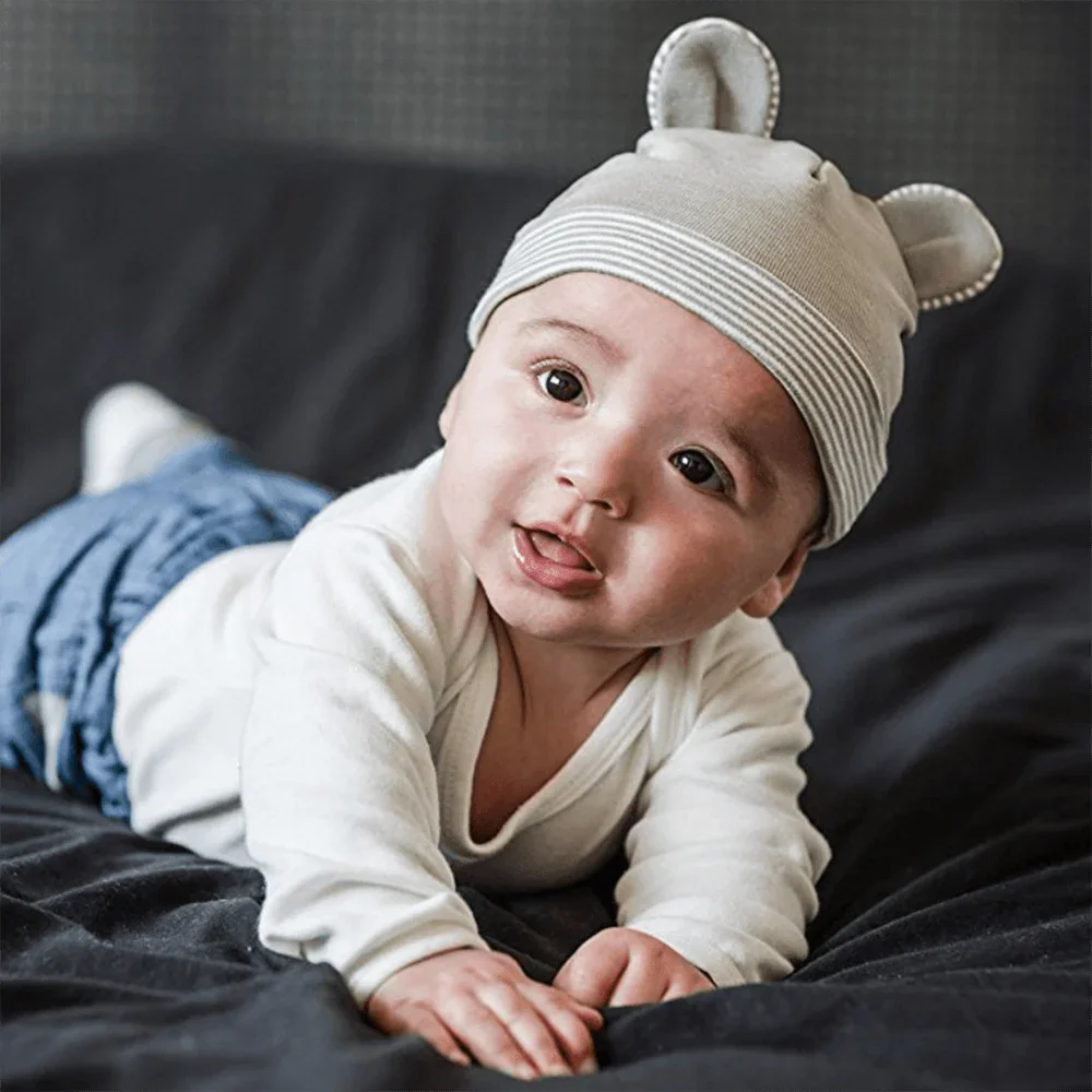 Baby lying on a blanket wearing a gray Belly Armor EMF protection hat