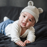 Baby lying on a blanket wearing a gray Belly Armor EMF protection hat