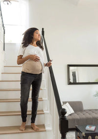 Pregnant woman standing in a studio wearing a beige Belly Armor EMF belly band