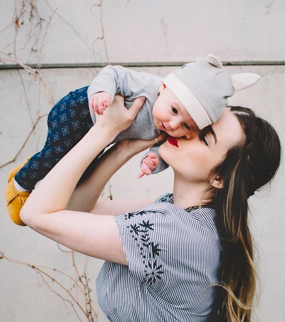 Mother lifting her baby wearing a Belly Armor organic cotton EMF protection hat