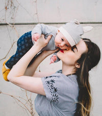 Mother lifting her baby wearing a Belly Armor organic cotton EMF protection hat